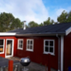 Udvendigt billede af et rødt hus med nyt tag, omgivet af træer og blå himmel.