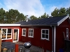 Udvendigt billede af et rødt hus med nyt tag, omgivet af træer og blå himmel.
